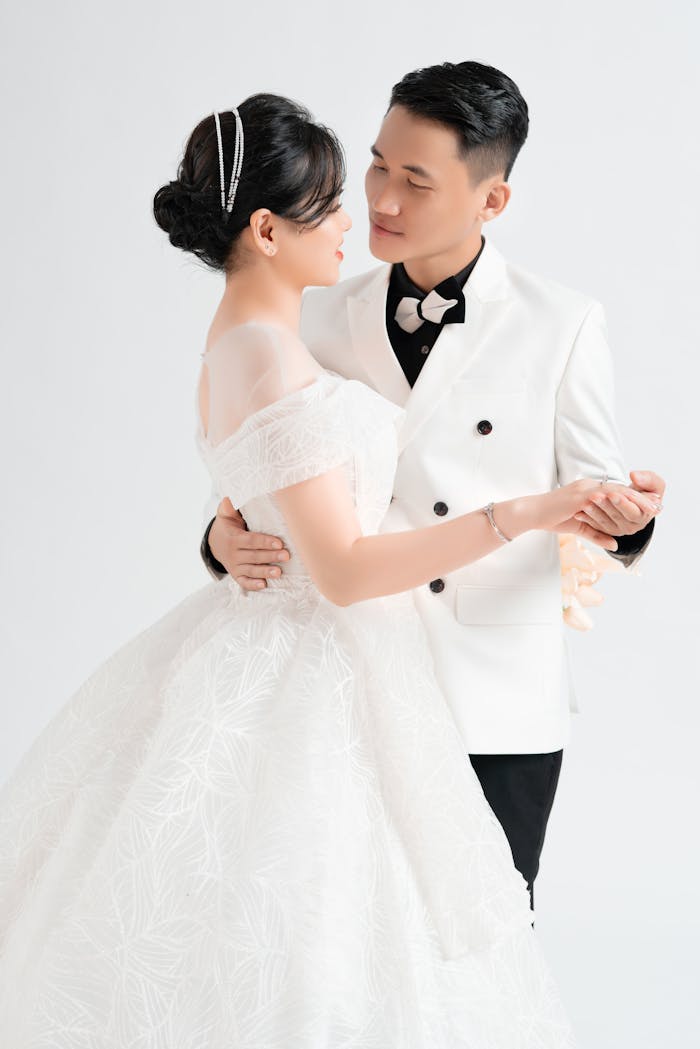 Home An elegant Asian couple shares a romantic dance in wedding attire, embracing their love.