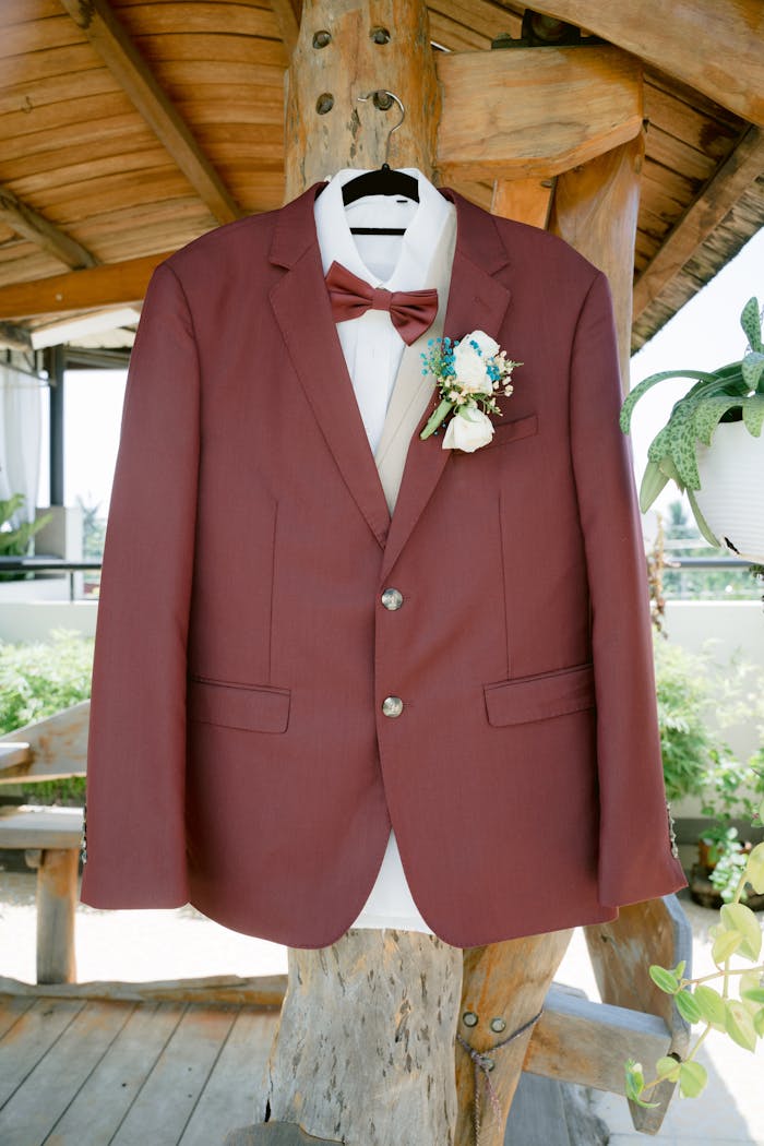 Home Close-up of a stylish burgundy suit with floral boutonniere hanging on a wooden post.